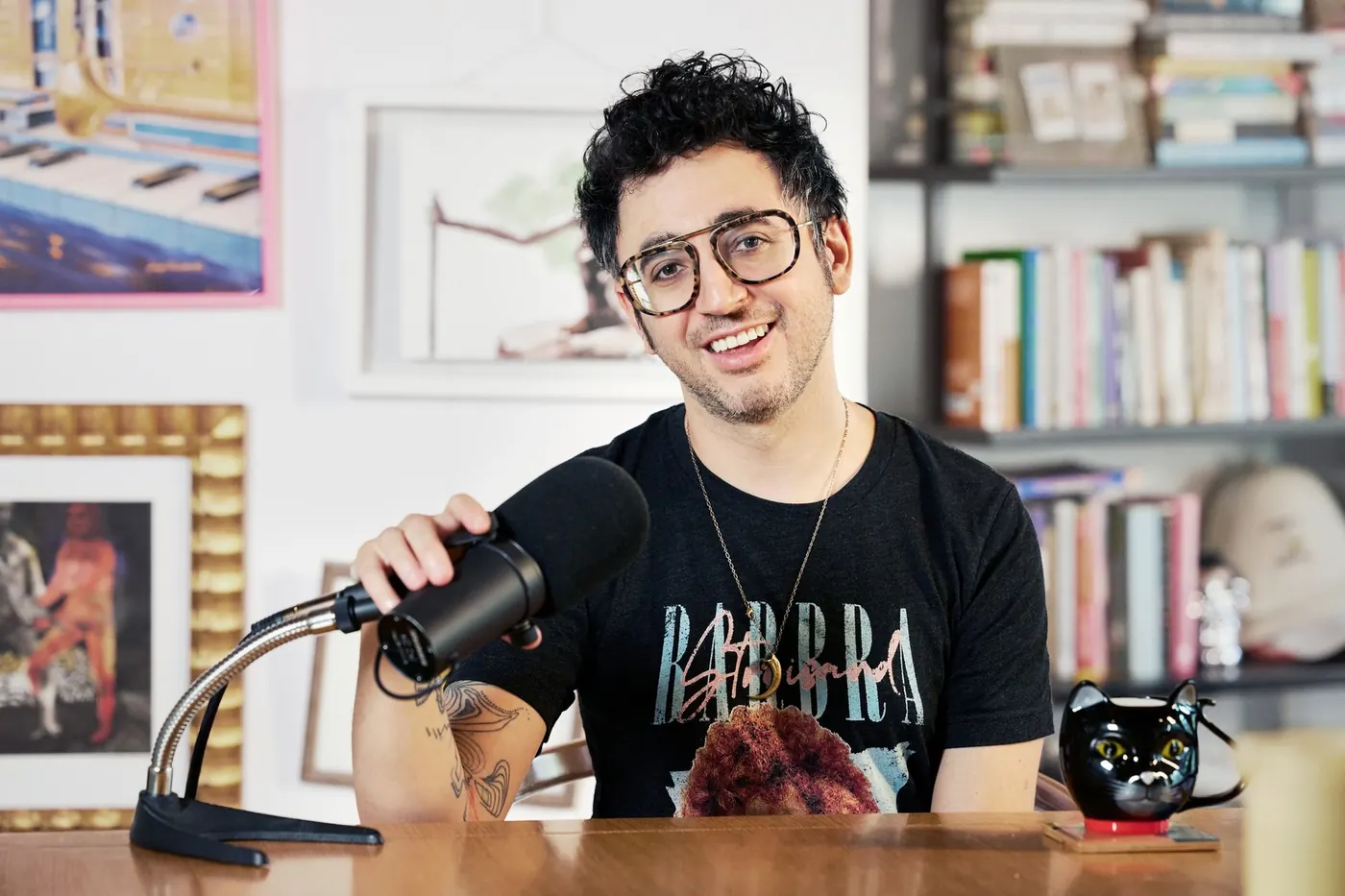 David Cooper at his desk with a microphone, a black cat mug and a bookshelf behind him